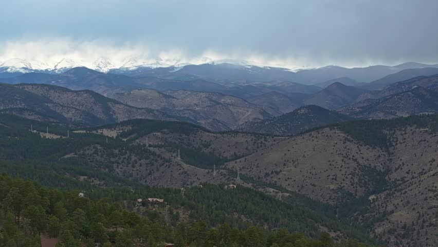 Panoramic aerial estabilshing overview of sweeping valleys covered and dotted with evergreen trees under stormy sky