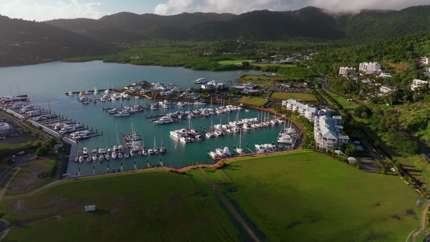 Port of Airlie Beach Bay Lagoon heart of Great Barrier Reef Whitsundays Whitehaven aerial drone green grass field sunny Coral Sea marina jetty Boathaven Beach sailboats cars buildings forward upward