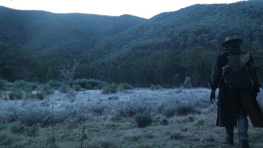 A traditional Australian bushman walks through a frosty ice valley during winter in the Australian mountains.