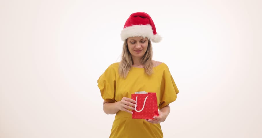Woman reaches into gift bag pulling out money with look of great surprise. Person in Christmas hat expresses strong joy waving money excitedly in hand