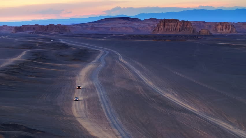 Aerial view of two off road vehicles kicking up dust on desert tracks through yardang formations at dusk