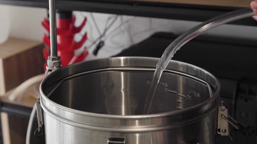 Water pouring into and filling up a metal pot in a home beer brewing setup, close up