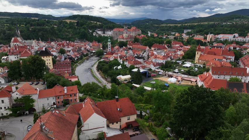Český Krumlov, South Bohemia, Czechia, July 2023. Drone aerial overview of idyllic town as visitors walk along quiet streets with Castle Tower and Chruches of St. Jost and St. Vitus in the distance.