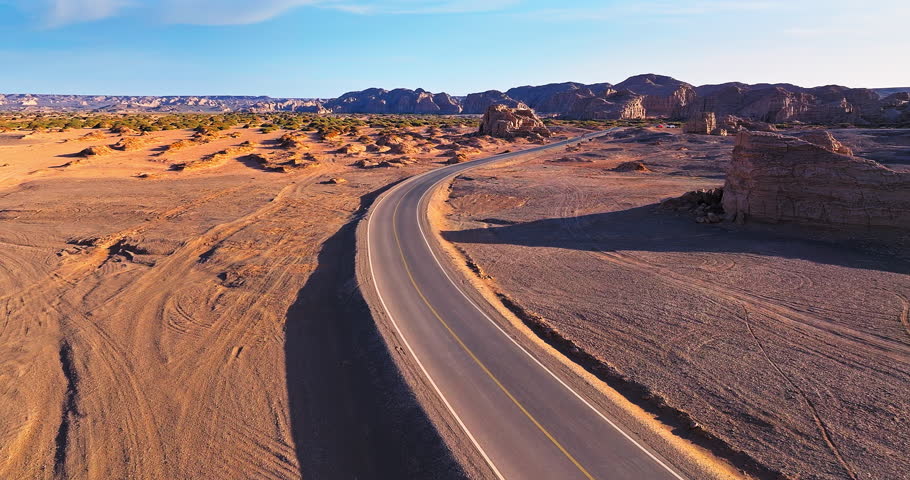 Aerial view of a winding asphalt road through a remote desert landscape with sandstone formations at sunrise