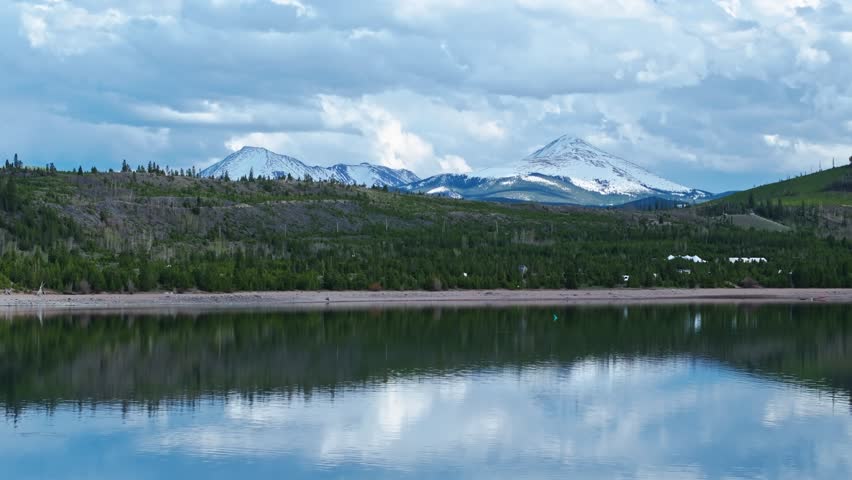 Drone rises above Dillon Reservoir to reveal evergreen forest and snowcapped peaks of Frisco Colorado