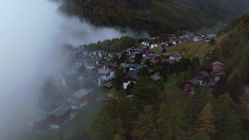 Moody fog Saastal Saas Fee village town Switzerland aerial drone foggy cloudy rainy Larch forest beautiful Fall Autumn Swiss Alps mountain peaks glacier valley Zermatt The Matterhorn forward reveal