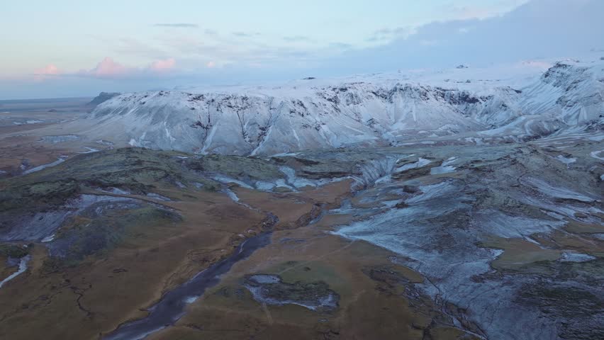 Aerial view of Mýrdalur, Iceland, featuring snow dusted mountains and valleys with winding streams and lush terrain.