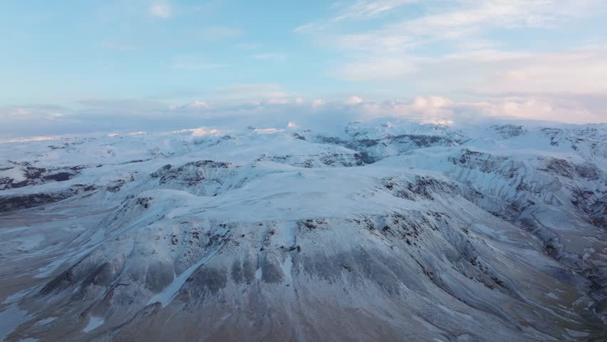 Aerial view of Mýrdalur, Iceland, showcasing a vast snow covered mountain range under a clear blue sky.