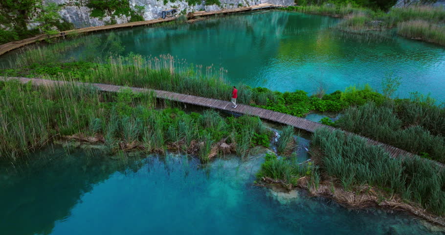Man Walking On Wooden Path Between Lakes Early Morning In Plitvice Lakes National Park, Croatia. orbiting drone shot