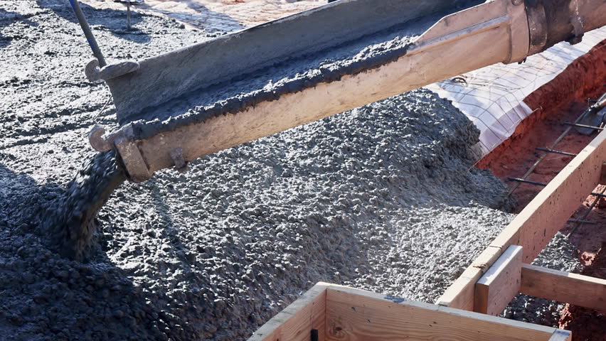 Workers pour fresh concrete foundation slab into wooden forms at construction site