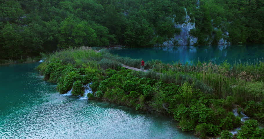 Man Strolling On Walkway Through Lakes With Small Waterfalls In Plitvice Lakes National Park, Croatia. orbiting drone shot