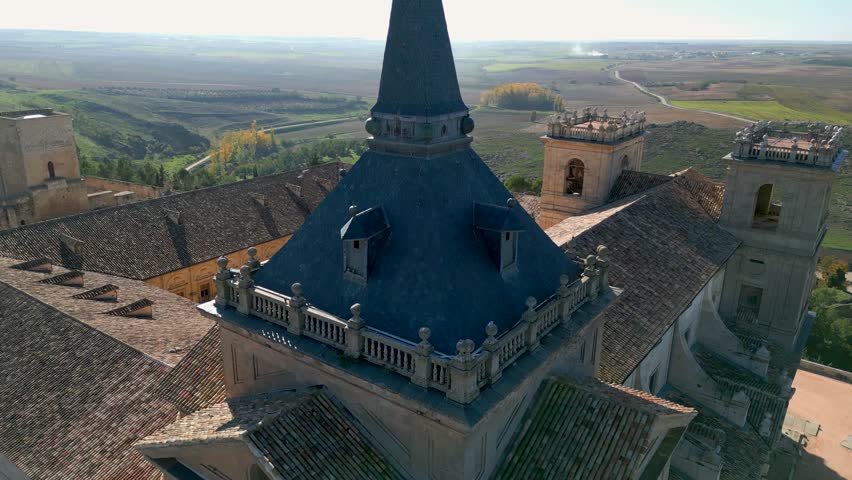 drone flight of the Ucles monastery seeing as the central image the black roof of the church tower located on one side with a beautiful landscape in the background in the province of Cuenca
