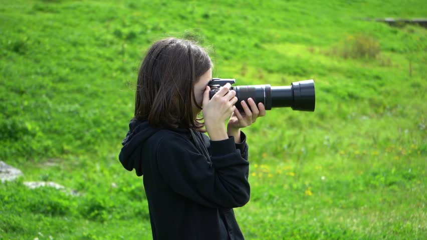 11 year old white girl is taking photos with a photo camera outdoor in the green park