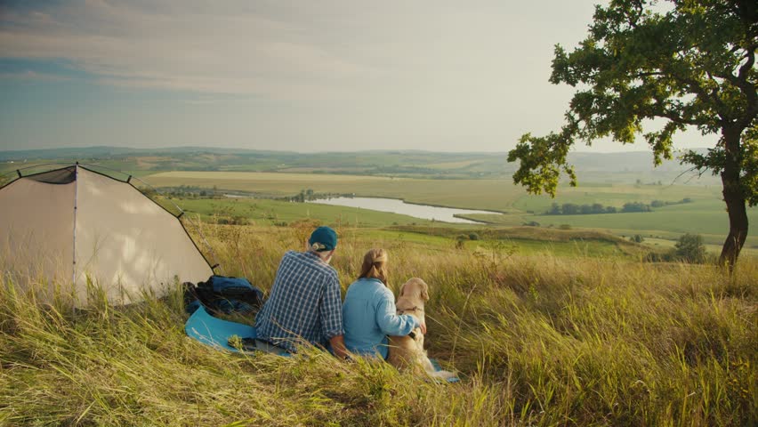 Pet-Inclusive Family Time. Senior Man Sits With His Family and Dog by a Tent, Admiring the Beautiful Landscape. A Peaceful Moment of Togetherness, Nature, and Joyful Living With a Beloved Pet