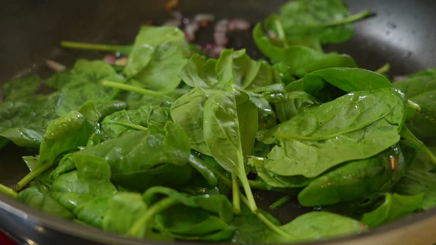 Stirring fresh spinach and caramelized onions on a black pan