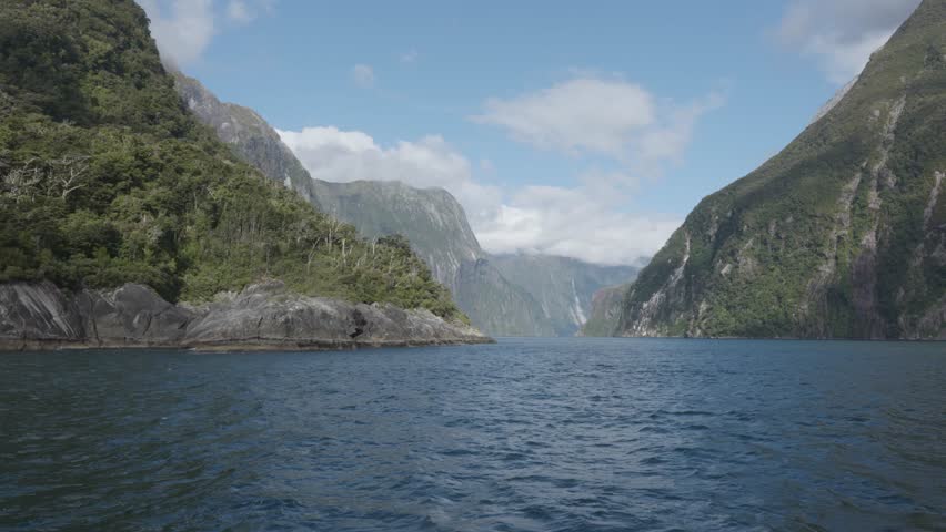 Wide view of the fiord and mountains from a boat during a sunny summer day in Milford Sound, Fiordland, New Zealand.