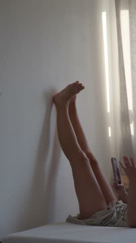 A Relaxed Woman Sitting on the Bed with Her Legs Up Against the Wall in a Calm Atmosphere
