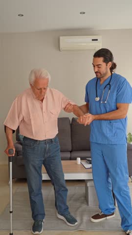 Vertical video of male Physiotherapist helping elderly man with walking at home
