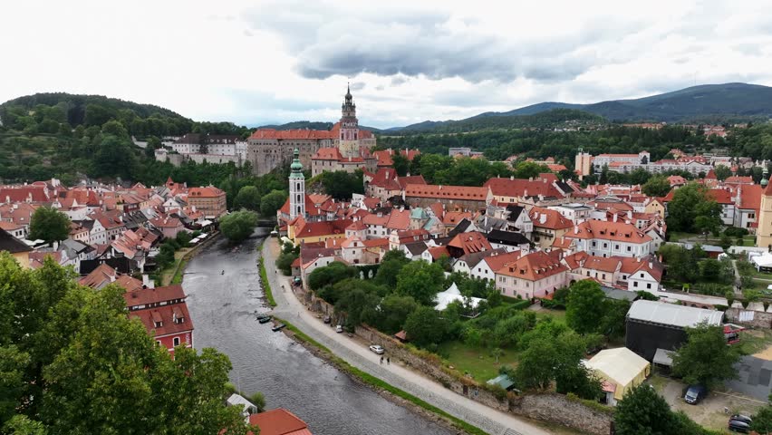 Český Krumlov, South Bohemia, Czechia, July 2023. Drone pushes forward above trees and Vltava river to establish the Church of St. Jost and medieval castle.