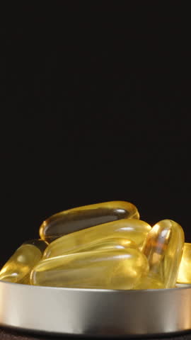 Vertical video. Looping 360-Degree Rotation of a Bottle Cap Filled with Omega 3 Capsules in Front of a Transparent Brown Glass Bottle Against a Dark Background