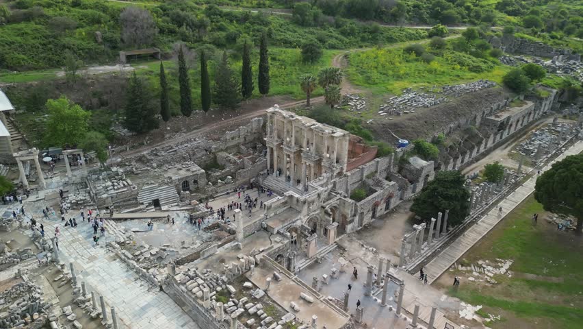 Aerial view of the main Ephesus amphitheater in Turkey. Concentric rows of seating lead to stage. Ancient walls and ruins remain. Surrounding greenery highlights site