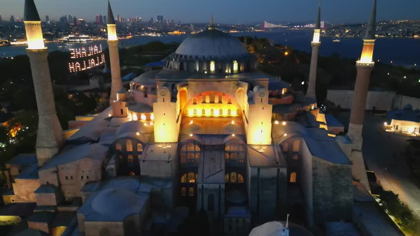 The drone lifts away from Hagia Sophia revealing its majestic structure. Behind, the lights of the Golden Horn glisten, blending history with Istanbul