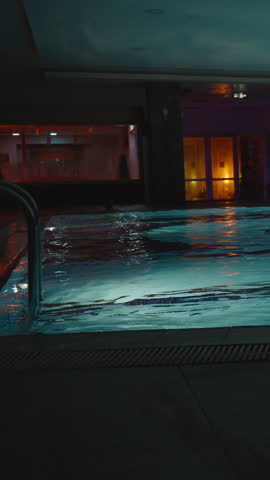 Vertical video. Spacious Indoor Pool with Blue Water Illuminated by Soft Ambient Lighting, Featuring Large Support Columns and Pool Ladders, Captured from a Wide-Angle Perspective, Luxury Wellness Con