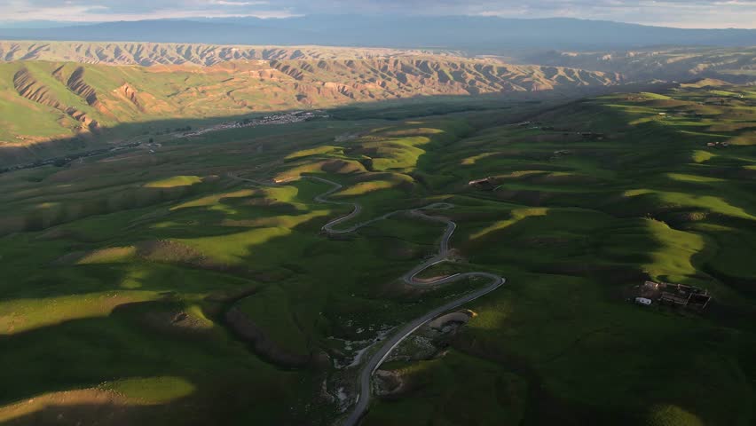 Winding mountain road through lush prairie landscape at sunset