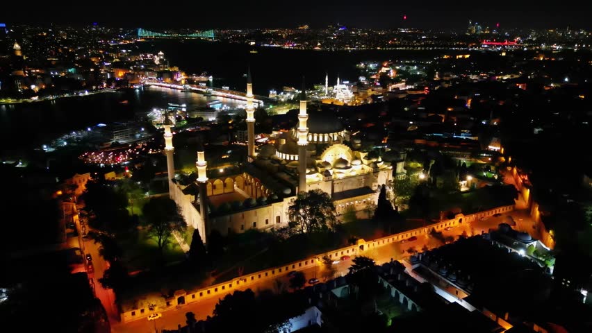 Stunning aerial photo of Suleymaniye Mosque lit up at night. The view extends toward the Golden Horn. The vibrant city lights enhance the historic architecture and serene Bosphorus
