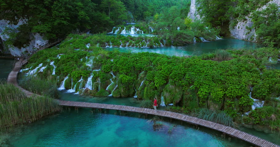 Man Over Wooden Hiking Trails Through Lakes And Green Forest Of Plitvice Lakes National Park In Croatia. Aerial Shot