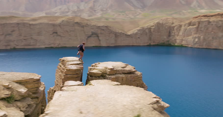 Man Over Towering Lakeside Cliffs Of Band-e Amir National Park In Afghanistan. Aerial Orbiting Shot