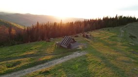 Aerial shot of serene sunset over hilly landscape in Ukraine. Rustic wooden cabin and dirt path nestled among rolling green hills, with forest and mountains bathed in warm, golden light. - Powered by Shutterstock - Get 15% off with code: PIKWIZARD15