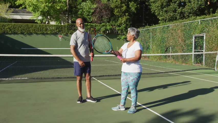 Mature man and senior woman exchanging high‑five on tennis court, with health icons and VHS glitch. Athletic, active, vibrant, energetic, companionship, outdoor, leisure