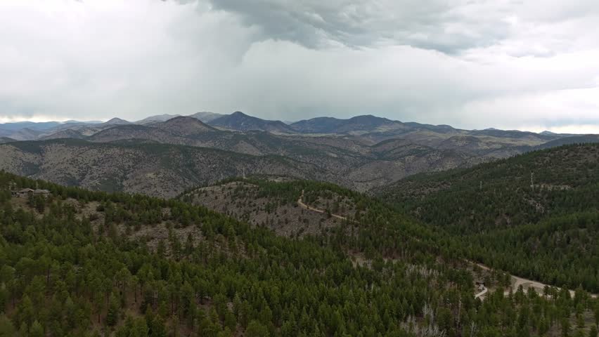 Aerial pullback above Rocky Mountains covered in evergreen trees creating natural forested landscape pattern