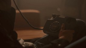 Young man holding vintage corded telephone and talking, sitting on sofa in living room filled with hazy warm light and blurred television in background. Tilt-up shot - Powered by Shutterstock - Get 15% off with code: PIKWIZARD15