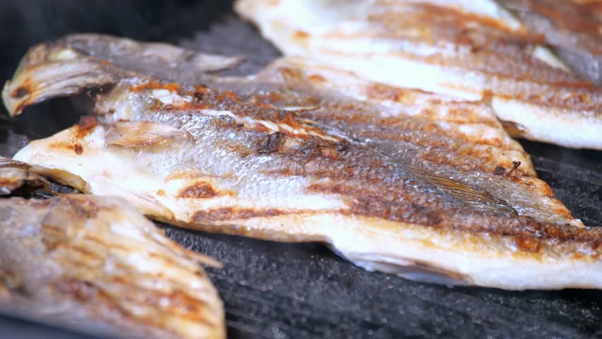 Grilling fish over open flames at a seaside location