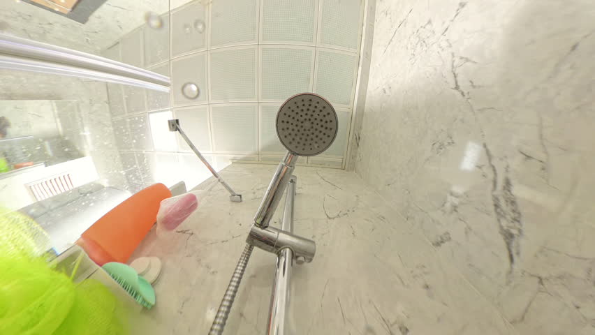 Vertical video. Water Spraying from Showerhead in Modern Bathroom with Marble Walls and Colorful Bath Items Visible, Captured in Close-Up from Below Hygiene and Shower Routine