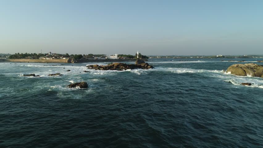 Waves crash on rocks at Galle Fort coastline, Sun setting over Sri Lanka Aerial View