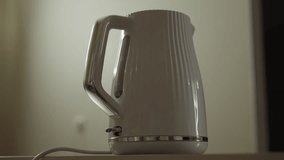 Finger pressing power button on white electric kettle, initiating brewing process near contemporary kitchen countertop. Close-up of man starting water boiling process for morning tea or coffee brewing - Powered by Shutterstock - Get 15% off with code: PIKWIZARD15