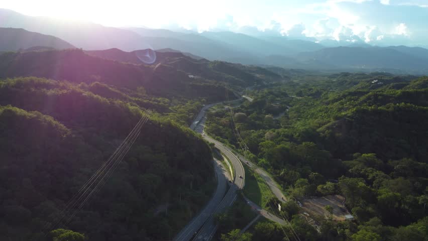 Drone view of a winding highway in the Colombian mountains at golden hour, with long shadows from the hills casting over the road. Dramatic natural scenery at sunset. uraba antioqueño santafe de antio