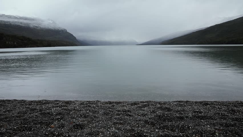 Raining in the lake. Panorama view of the calm lake, hills and forest under a cloudy sky. The drops of water fall into the lake's surface
