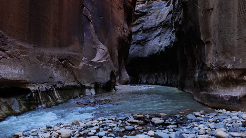 Slow pan to the left following the Virgin river as it flows inside the Narrows at Zion National park in Utah, USA. 