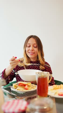 Young woman eating breakfast with crepes, strawberries, honey and tea, isolated on white background