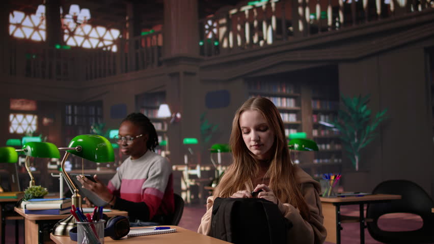 Focused girl arriving at university library and opening textbook to write notes, doing research with the help of massive books database at campus designated space for self learning. Camera B.