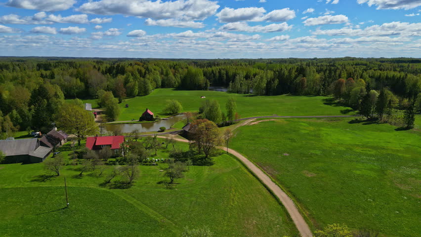 Scenic view of red houses beside a circular pond on a sunny day amidst Latvia
