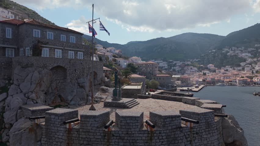 An orbit drone shot around the Miaoulis Monument at Hydra’s port reveals the island’s seafront promenade with traditional buildings and coastal charm