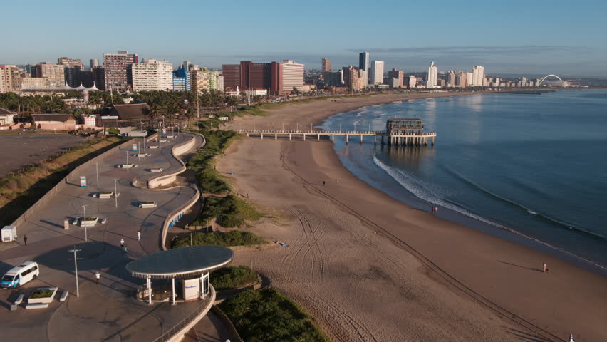 An early morning drone aerial captures Durban’s South Beach and Golden Mile, moving from the Beach Club along the quiet shoreline as waves roll onto the sand in the soft morning light.