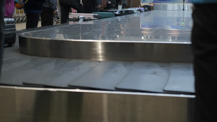 Bags and suitcases glide along the luggage carousel, revealing a variety of colors and designs. Travelers eagerly await their belongings in airport environment. Selective focus