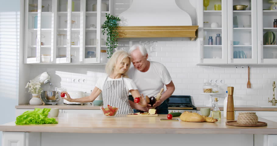 Positive old man and woman listening to music and dancing in kitchen, portrait. Good mood and emotions, have fun together, retirees feeling good and enjoying life, happy elderly spouses moving funny
