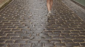 A cobblestone street, glistening with moisture, stretches ahead as a person walks away. The person's lower legs and feet are visible, clad in casual sneakers, emphasizing movement and exploration. - Powered by Shutterstock - Get 15% off with code: PIKWIZARD15